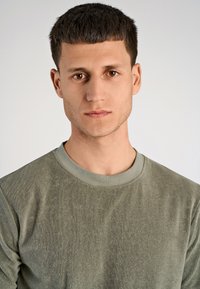 Camicia verde a maniche lunghe con un tessuto testurizzato, caratterizzata da un collo a girocollo di un verde più chiaro e una vestibilità comoda. Chiara attenzione al capo.