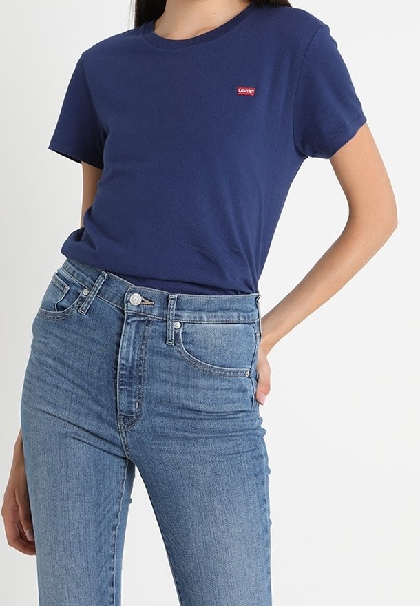 Marineblaue Baumwoll-T-Shirt mit kurzen Ärmeln, versehen mit einem roten Levi's-Logo. Kombiniert mit hellblauen hochgeschnittenen Jeans.