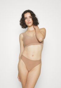 Lys beige sømløs bralette med V-hals og tynne stropper, parret med matchende høytaljede bikinitruser. Glatt, elastisk stoff.