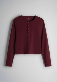 Top tricotat, bordo închis, cu mâneci lungi, cu gât rotund și o fenta cu cinci nasturi pe un fundal deschis.