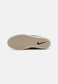 Súťažná obuv Nike, podrážka z textúrovanej gumy v béžovej farbe, s výrazným hnedým dizajnom swoosh a geometrickým vzorom pre trakciu.