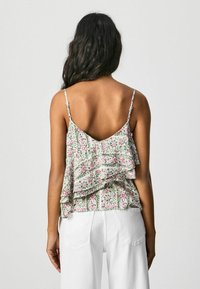 Camisole met bloemenprint, voorzien van gelaagde ruffles, verstelbare spaghettibandjes en een V-vormige achterkant. Gecombineerd met witte broek.