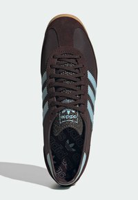 Dark brown sneaker with light blue three-stripe design, textured black tongue, and patterned insole. Lace-up style and rubber sole.