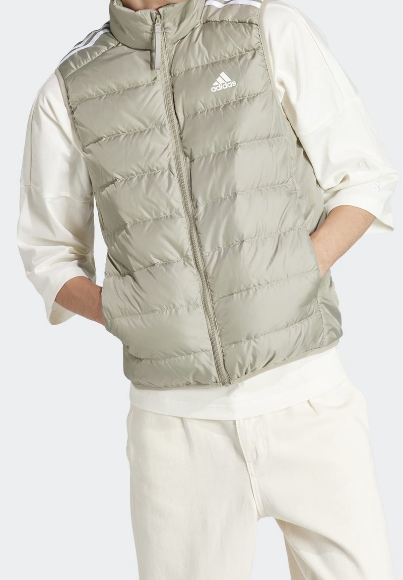 Pohodlná vesta v světlé olivově zelené barvě, vyrobená z lesklého materiálu se zipovým zapínáním a vysokým límcem. Obsahuje bílé logo Adidas a kontrastní pruhy.