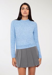 Maglione azzurro chiaro in morbido maglione a maniche lunghe e scollo rotondo abbinato a una gonna grigia a pieghe. Texture liscia, design informale.