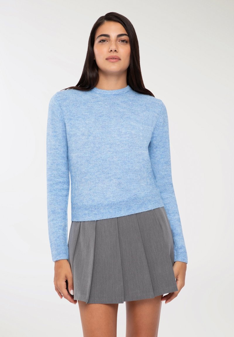 Maglione azzurro chiaro in morbido maglione a maniche lunghe e scollo rotondo abbinato a una gonna grigia a pieghe. Texture liscia, design informale.