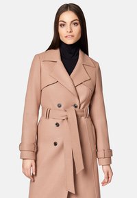 Jasnoróżowy płaszcz trench z podwójnymi guzikami, szerokimi klapami i paskiem w talii. Miękka tkanina z usztywnionymi rękawami i mankietami.