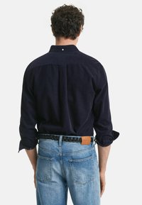 Marinblå kordflamskjorta med uppvikta ärmar, enkel bröstveck, bärs med ljusblå denimjeans och ett svart flätat bälte.