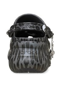 Schwarze und graue Leopardenmuster-Crocs mit einem schwarzen Riemen, ausgestattet mit einem Yin-Yang-Anhänger und strukturierten Oberflächen auf der Rückseite.