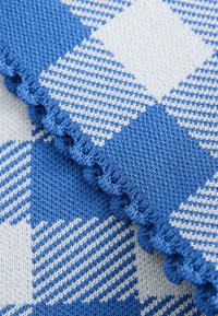 Tela de punto en cuadros azules y blancos con patrones variados; presenta un borde texturizado con un ribete festoneado.