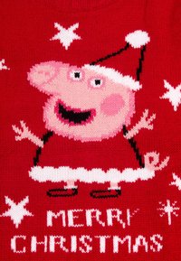 Maglione rosso a maglia con un maialino cartone animato rosa in un cappello di Natale, circondato da stelle bianche, con "BUON NATALE" in testo bianco.