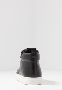 Czarny skórzany botek za kostkę o zaokrąglonym kształcie, z teksturowanymi panelami bocznymi, białą gumową podeszwą i tylnym uchwytem ułatwiającym zakładanie.