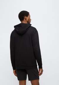 Μαύρο φούτερ με κουκούλα και μακριά μανίκια, με ομαλή υφή, ίσια γραμμή, ορατές ραφές, συνδυασμένο με μαύρο σορτς.