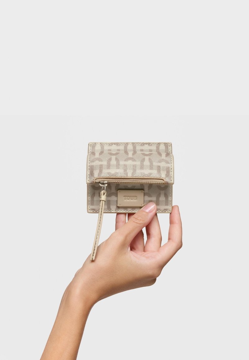 Beige wallet with a patterned exterior, curved top, zipper closure, and a wrist strap. Features a small logo detail on the front.