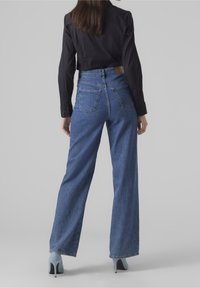 Jeans in denim blu a vita alta, dal taglio morbido; dotati di cinque tasche e di un'etichetta in pelle marrone sulla cintura posteriore.