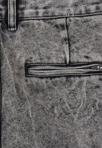 Denimbukser i svart og grått med en glidelåslomme og en teksturert overflate, med et subtilt stripemønster og standard beltehemper.