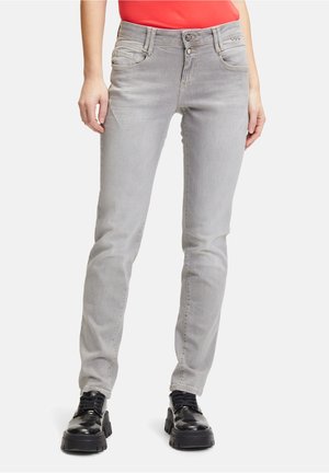 Jeans skinny gris avec cinq poches, présentant un délavage légèrement usé, une fermeture à bouton et des coutures contrastées. Associés à des chaussures noires à semelles épaisses.