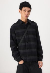 Black and grey plaid shirt jacket with a button front, collar, and long sleeves. Features a textured fabric and a straight cut.