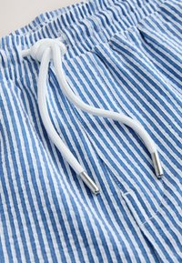 Blue and white vertically striped fabric with a white drawstring tied in a knot and metal tips.
