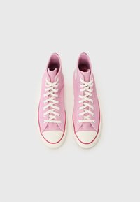 Pink canvas high-top sneakers with white laces, rubber toe cap, and a contrasting red sole. Smooth texture with minimal branding detail.