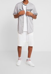 Jersey de béisbol gris con letras en negro que dicen "Chicago", combinado con pantalones cortos blancos. Los accesorios incluyen zapatillas blancas y calcetas a rayas.