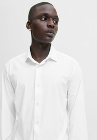 Camicia bianca a maniche lunghe con colletto classico, chiusura frontale con bottoni e tessuto liscio; presenta una consistenza morbida e una vestibilità casual.