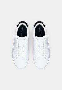 Baskets blanches avec une tige en cuir lisse, bout rond, lacets plats et col rembourré noir. Présente un logo sur la languette et sur le côté.