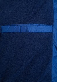 Gros plan sur un tissu en polaire bleu foncé avec une bordure en satin horizontale et un détail de couture le long du bord droit.