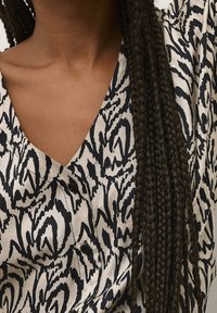 Blusa de botones en beige claro con un patrón abstracto negro, que presenta un escote en V, mangas cortas y tejido texturizado.