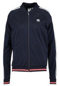 Námořnická bunda na zip vyroben á z měkké látky. Obsahuje bílé pruhy na rukávech a růžový akcent na spodním lemu. Má boční kapsy.