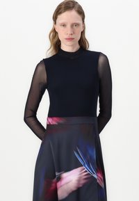 Haut à manches longues et col montant en tissu bleu marine uni, associé à une jupe fluide arborant un imprimé abstrait coloré dans des tons sombres.