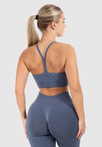 Sujetador deportivo gris con diseño de espalda cruzada, combinado con leggings de cintura alta. La textura suave y la forma ajustada mejoran la comodidad.