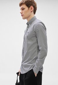 Πουκάμισο με κουμπιά, με στενές μαύρες και λευκές ρίγες, διαθέτει γιακά και ένα μικρό λογότυπο. Μακριά μανίκια με κουμπωτές μανσέτες, ελαφρώς εφαρμοστή γραμμή.