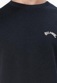 Maglione girocollo navy realizzato in morbido tessuto, con un piccolo logo bianco "Billabong" ricamato sul petto. Texture liscia, vestibilità modellata.