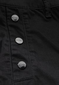 Tela negra con una textura suave, que presenta tres botones plateados brillantes con el logo de "StreetOne". Detalles de costura visibles.