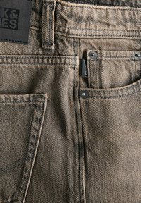 Džínsy z denimu v svetlohnedej farbe, s textúrovanou tkaninou, štandardnými vreckami, striebornými gombíkmi a značkovou etiketou prišitou na páse.