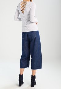 Haut à manches longues gris clair côtelé avec dos ouvert et détail croisé, associé à des culottes en denim bleu foncé mi-longues et des bottines noires.