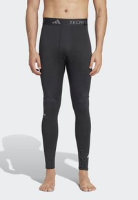 Leggings a compressione neri con una ampia fascia elastica in vita etichettata "TECHFIT". Presentano pannelli testurizzati nella parte bassa delle gambe. Finitura liscia complessiva.