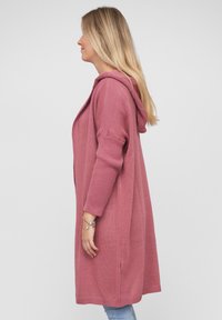 Lang hettere cardigan i myk rosa strikk. Har ribbestrikkede ermer og åpen frontdesign, som faller under hoftene.