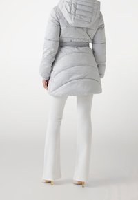 Lysegrå dunjakke med tekstureret mønster, elastisk talje og hætte. Kombineret med hvide vidde bukser og lyse sko med hæl.