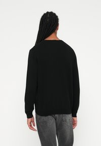 Zwarte sweater van zacht materiaal, met een ronde hals, lange mouwen en een ribbelboord. Draagt met grijze jeans, zichtbare eenvoudige achterkant.
