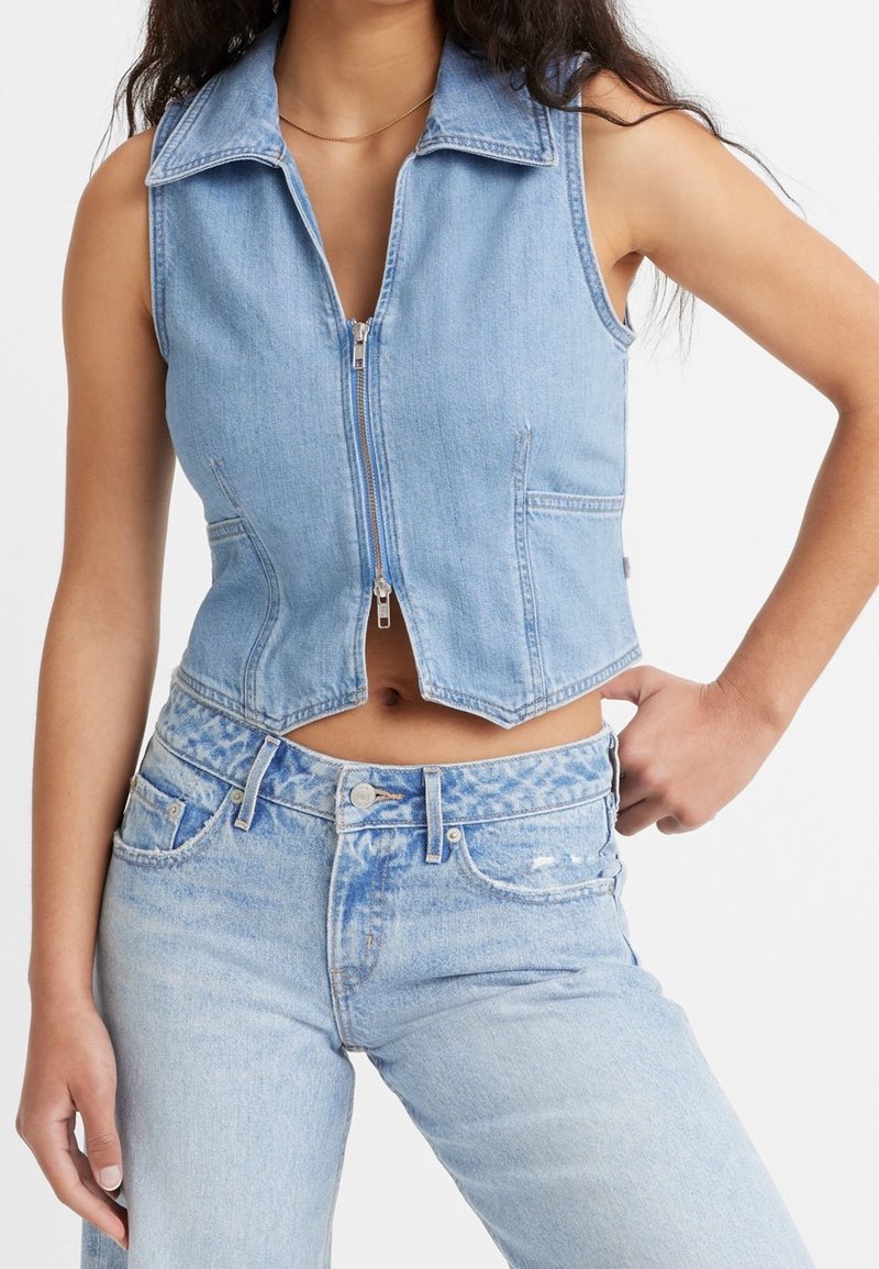 Ljusblå denimkort väst med dragkedja fram, krage och sidofickor, tillsammans med matchande högmidjade jeans som har ett blekt utseende.