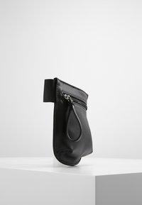 Musta vetoketjullinen pussukka, joka on tehty sileästä nahasta ja jossa on sivukahvalenkki sekä teksturoitu hihna yläosassa helppoa kantamista varten.