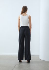 White sleeveless top paired with black wide-leg pants featuring an elastic waistband and side pockets, worn with black high-heeled shoes.