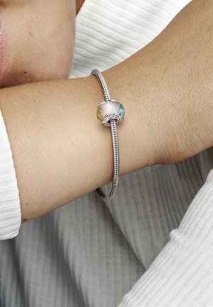 Silver bracelet featuring a central glass bead with a multicolored gradient, round shape, and a textured finish. Worn on an arm.