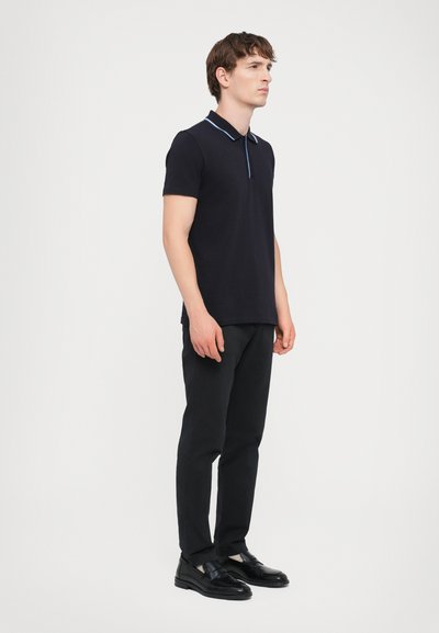 Camisa polo azul-marinho com um colarinho fino em azul claro, mangas curtas, combinada com calças pretas e sapatos pretos tipo slip-on. Design limpo, textura mínima.