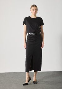 Camiseta de algodón negra de manga corta, combinada con una falda maxi de mezclilla negra con una abertura frontal y borde deshilachado, usada con tacones negros.