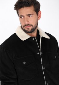 Fekete kordbársony kabát, krém színű shearling gallérral, elülső zsebekkel és patentos záródással. Puhább szövet, amely melegséget biztosít.