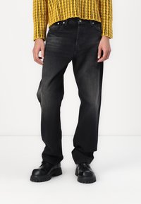 Czarne jeansy z denimu o luźnym kroju, z pięcioma kieszeniami i subtelnym przetarciem, połączone z żółtym swetrem o fakturze dzianiny i czarnymi butami.