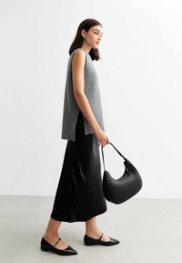 Grå ärmlös stickad topp med sidofickor, matchad med en svart satin maxi kjol. Modellen håller en böjd svart handväska med gulddetaljer.
